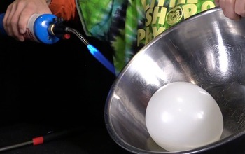 man holding a torch over a balloon in a metalic bowl